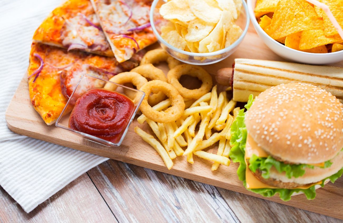 Einige fettige Sodbrennen-Verursacher wie Burger, Pommes und Pizza auf einem Holzbrett