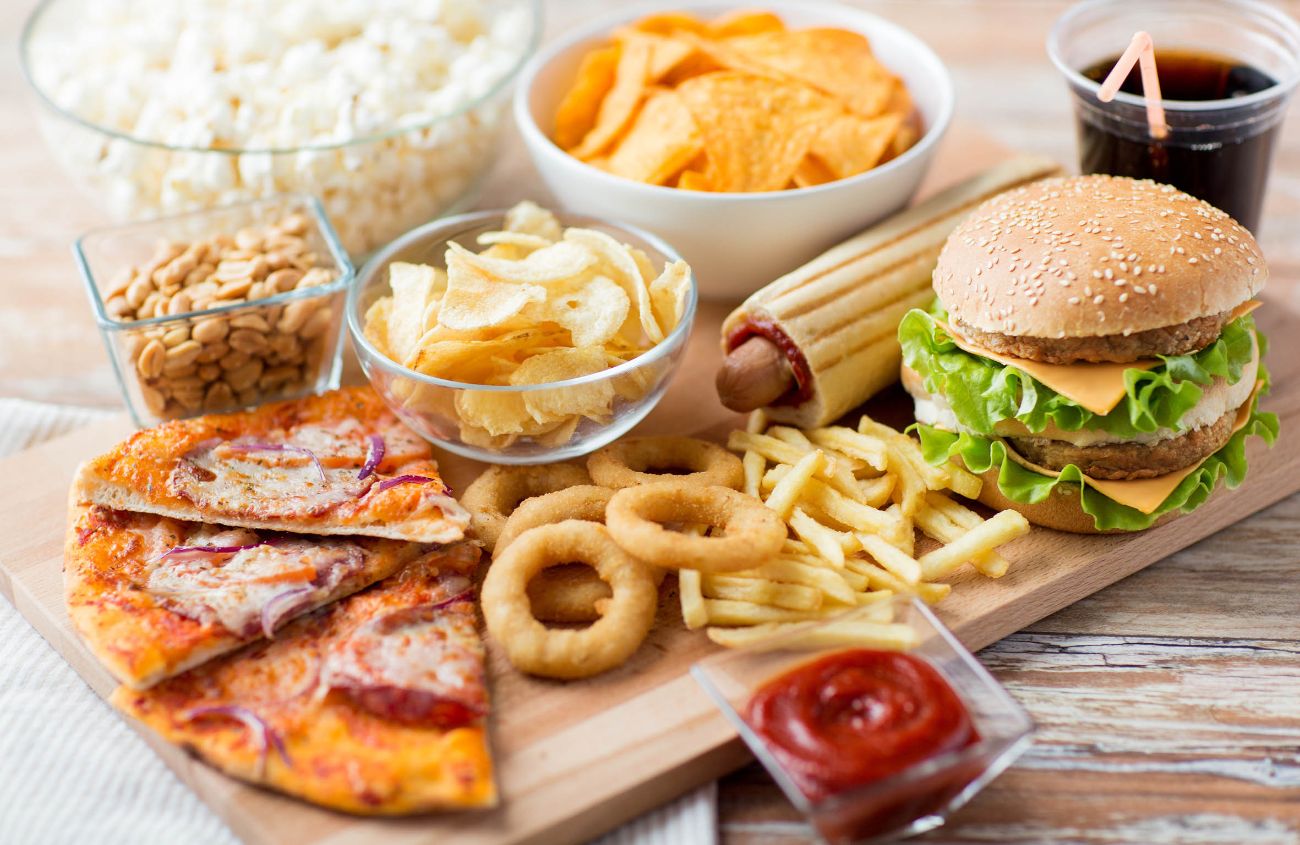 Holzbrett mit fettigem Essen wie Pizza, Burger, Pommes und Chips.