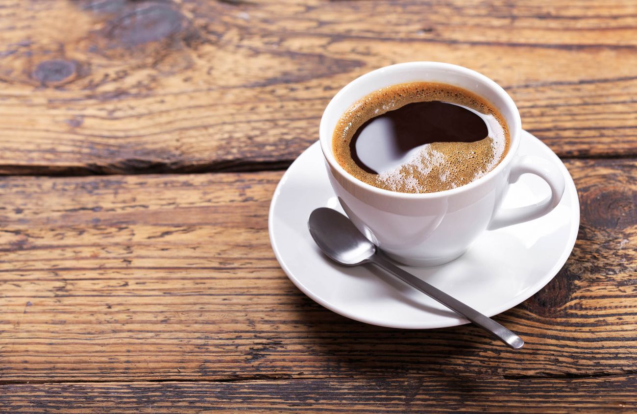 Tasse mit schwarzem Kaffee auf einem dunklen Holztisch.