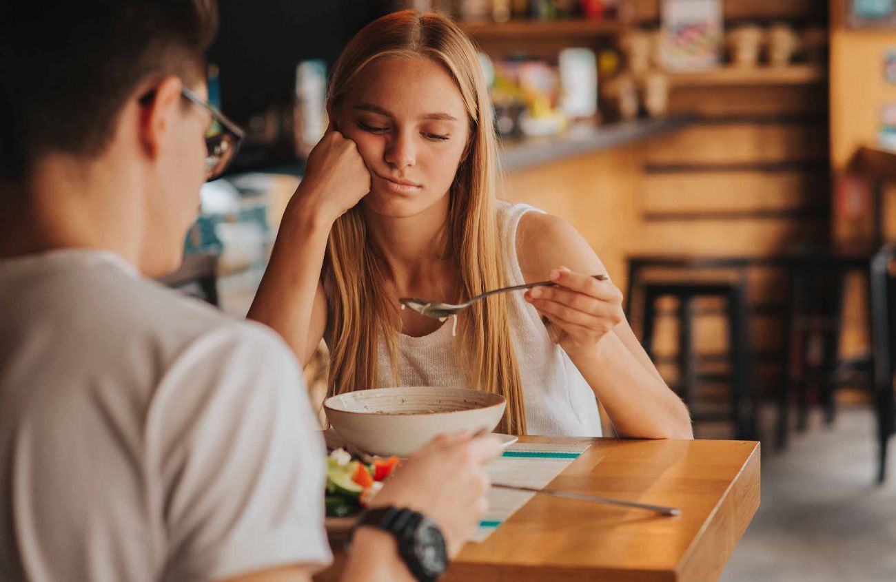 Bauchschmerzen, junge Frau sieht sich lustlos das Essen auf ihrem Löffel an