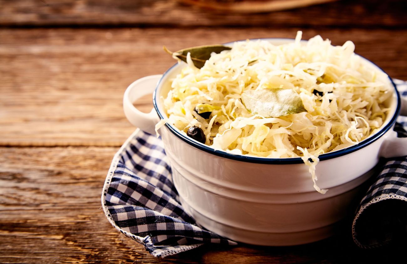 Weißer Topf mit Sauerkraut auf einem Holztisch.