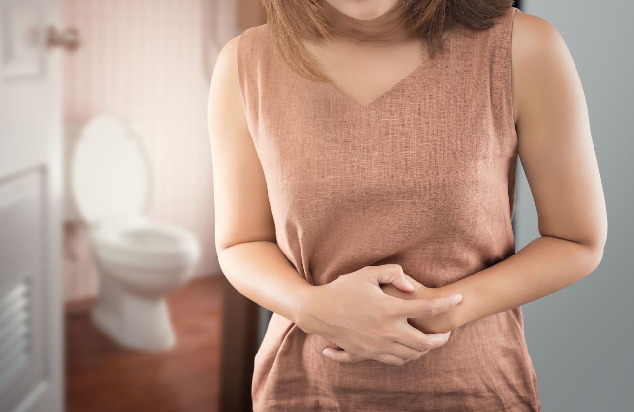 Durchfall, Frau hält sich den Bauch, im Hintergrund steht eine Toilette
