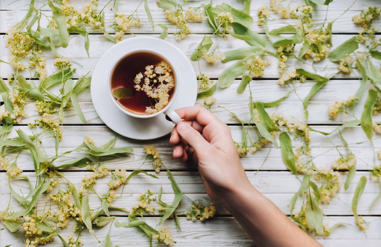 Hand greift nach einer Tasse Tee aus Lindenblüten. Das Konzept der Kräutermedizin. Behandlung von Erkältung und Grippe.