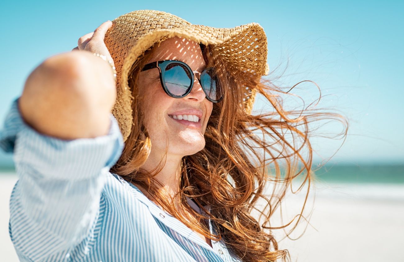 Durchfall im Sommer, Frau mit Strohhut und Sonnenbrille steht in der prallen Sonne