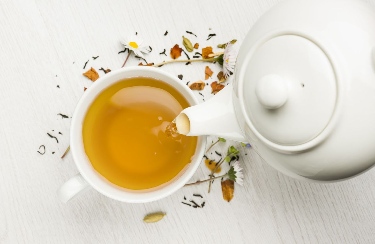 Magen-Darm-Entspannung, Draufsicht einer weißen Teekanne, die Kamillentee in eine Tasse schenkt