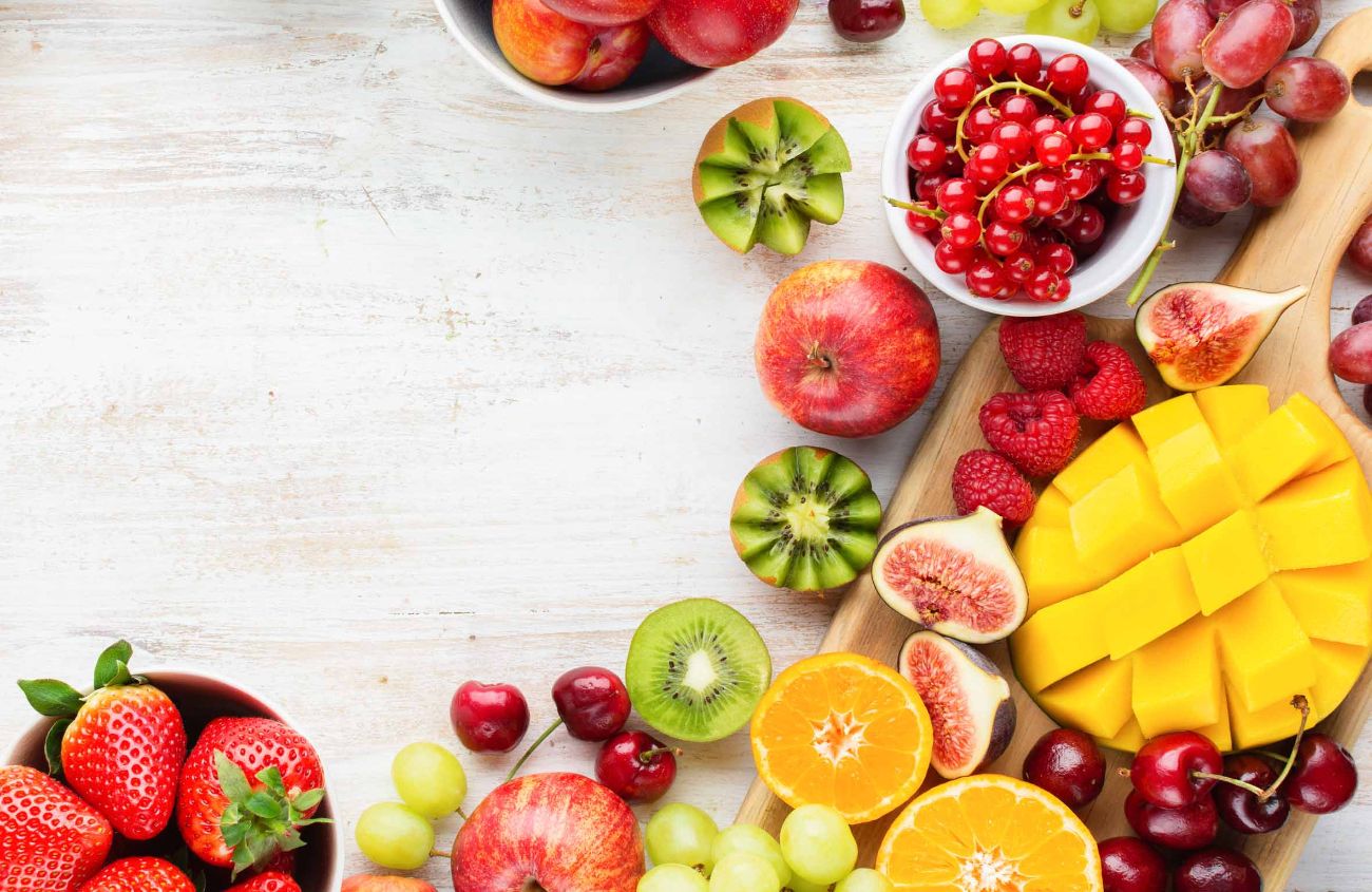 Unverträglichkeiten: Draufsicht auf geschnittene Mango, Erdbeeren, Himbeeeren, Orange, Pflaumen, Apfel, Kiwis, Trauben, Blaubeeren, Kirschen