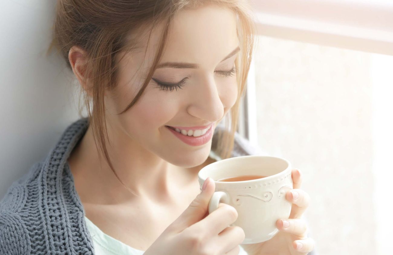 Frau lächelt mit einer Tasse Tee in den Händen