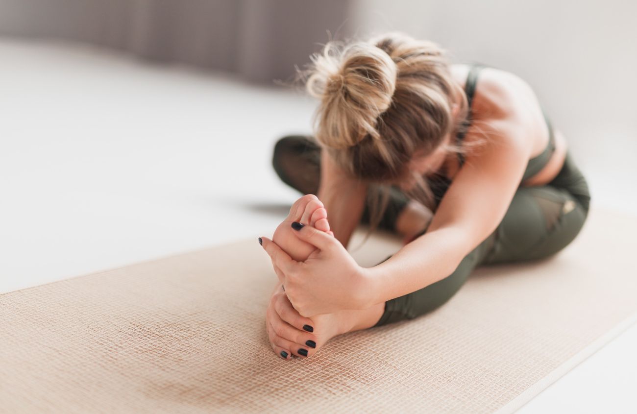 Gsatritis durch Stress, Frau macht Yoga im Sitzen und beugt sich zu ihrem Fuß vor
