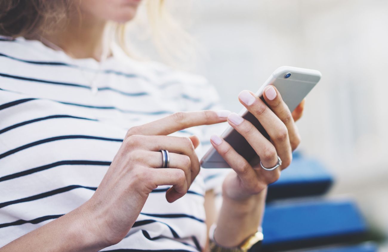 Frau hält ihr Smartphone in der Hand und wischt darüber.