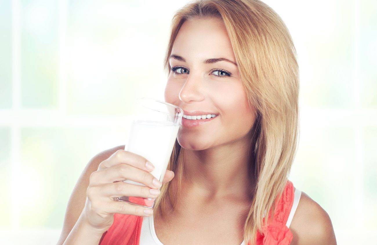 Frau führt sich Glas mit Milch-Alternative zum Mund