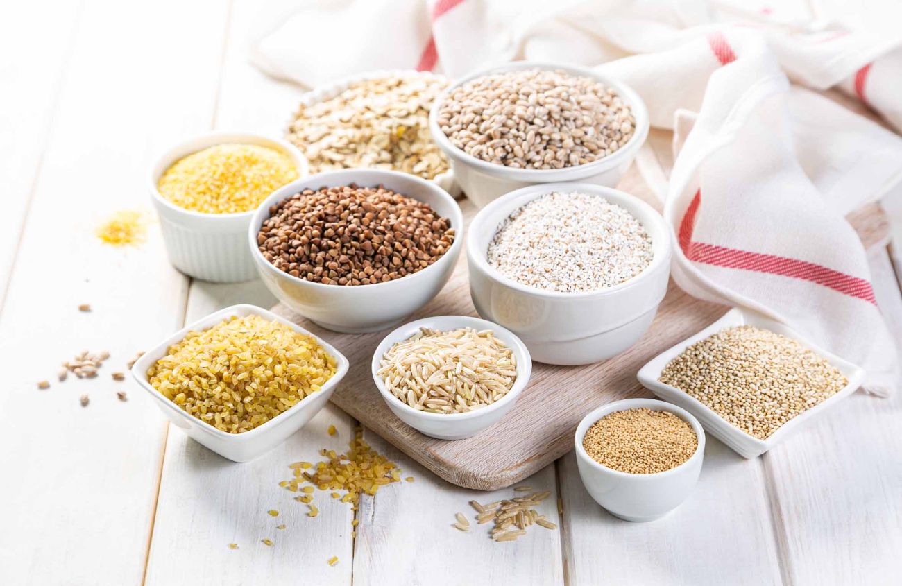 Auswahl von Körnern in weißen Schüsseln - Reis, Hafer, Buchweizen, Bulgur, Brei, Gerste, Quinoa, Amarant, auf weißem hölzernem Hintergrund