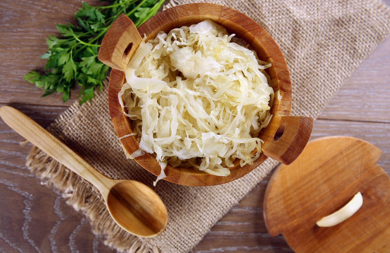 Eine Schüssel mit Sauerkraut steht auf einem Tisch, daneben liegt ein Holzlöffel.