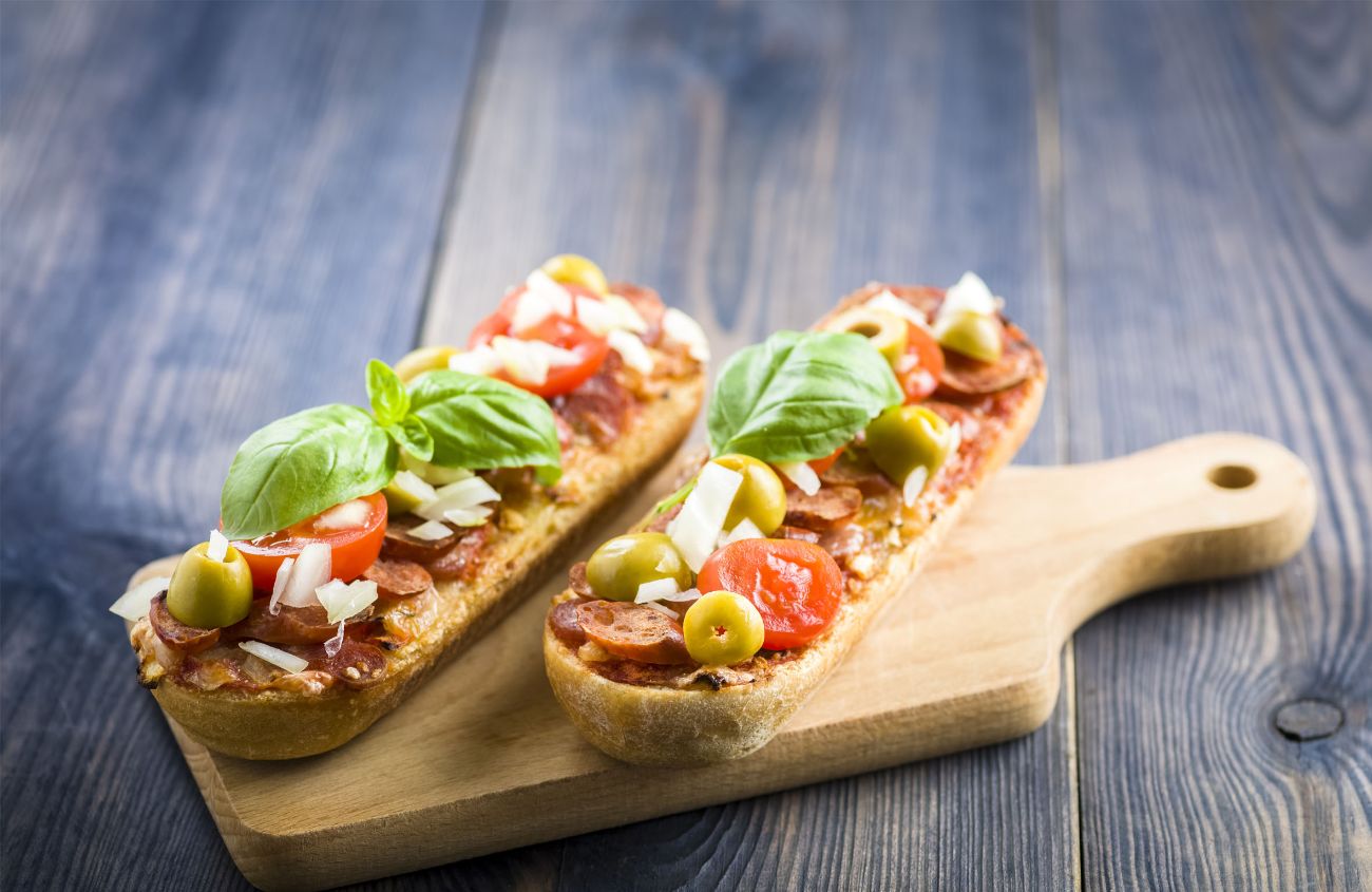 Zwei Bruchetta mit Pizzabelag auf einem Holzbrett.
