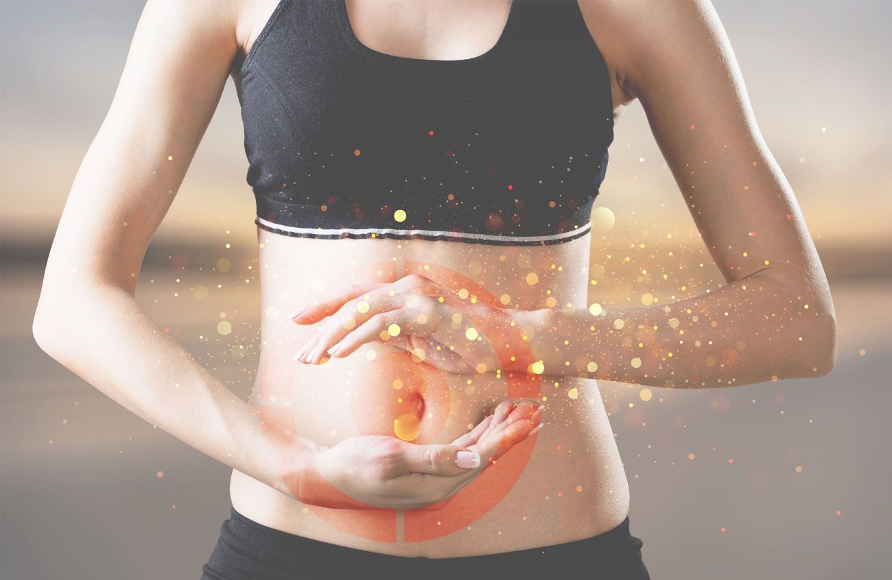 Frau in einem Sportoberteil hält die Hände schützend vor ihren Bauch.