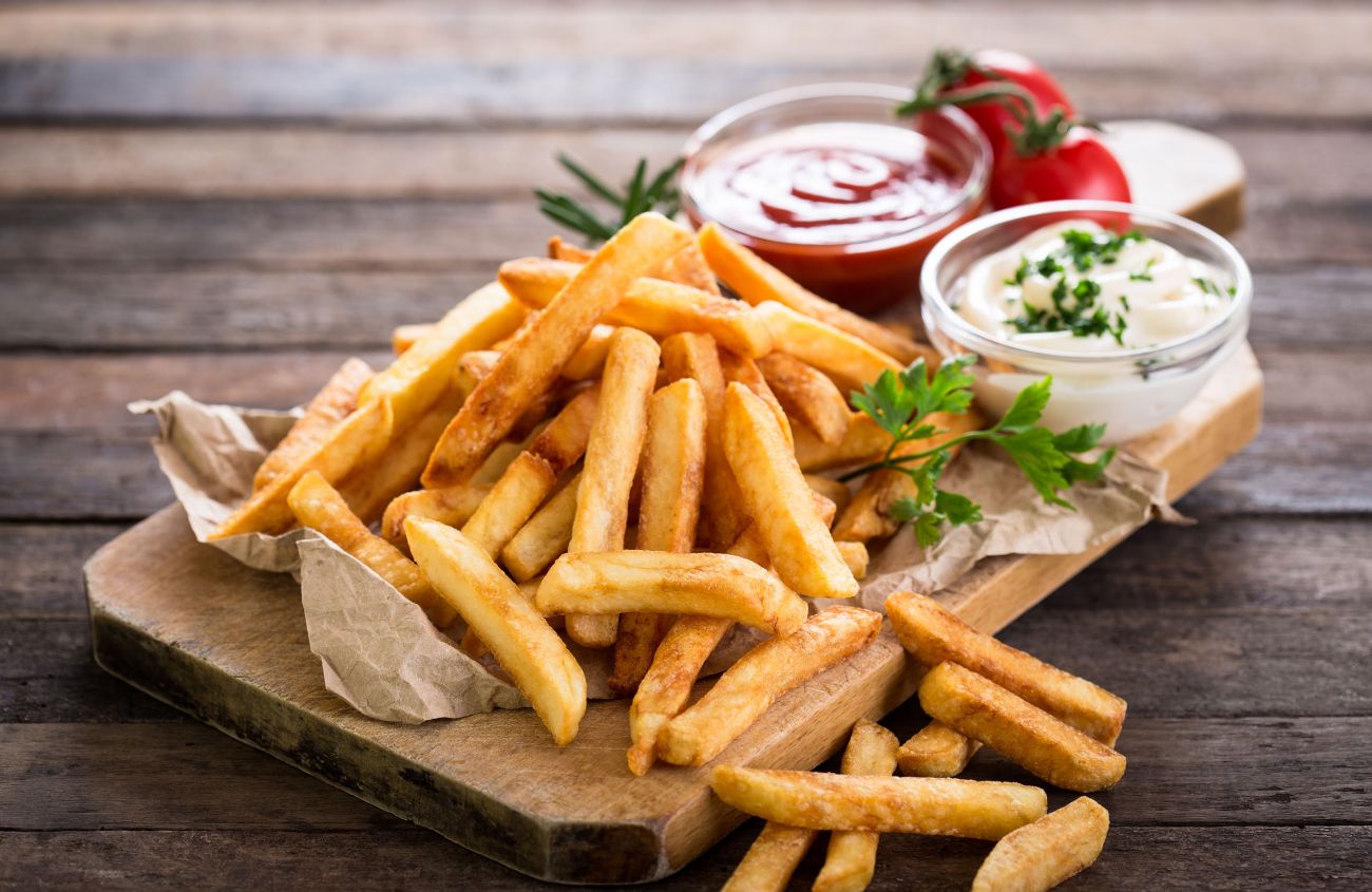 Pommes und verschiedene Dips auf einem Holzbrett.