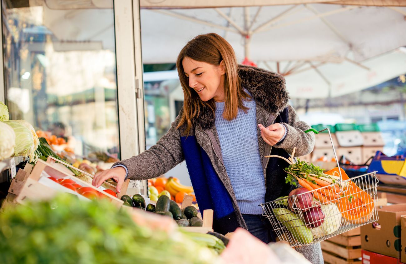 Frau steht vor der Gemüseabteilung im Supermarkt und kauft Rohkost.