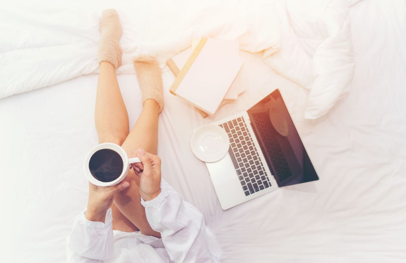 Ursache von Schlafstörungen, Frau liegt im Bett und trinkt Kaffee