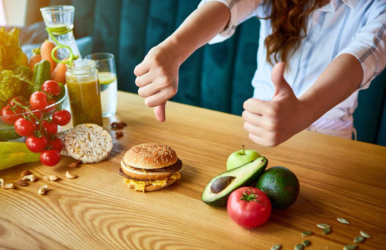 Ernährung bei Sodbrennen, Frau lehnt ab, Hamburger zu essen, und greift zum Gemüse