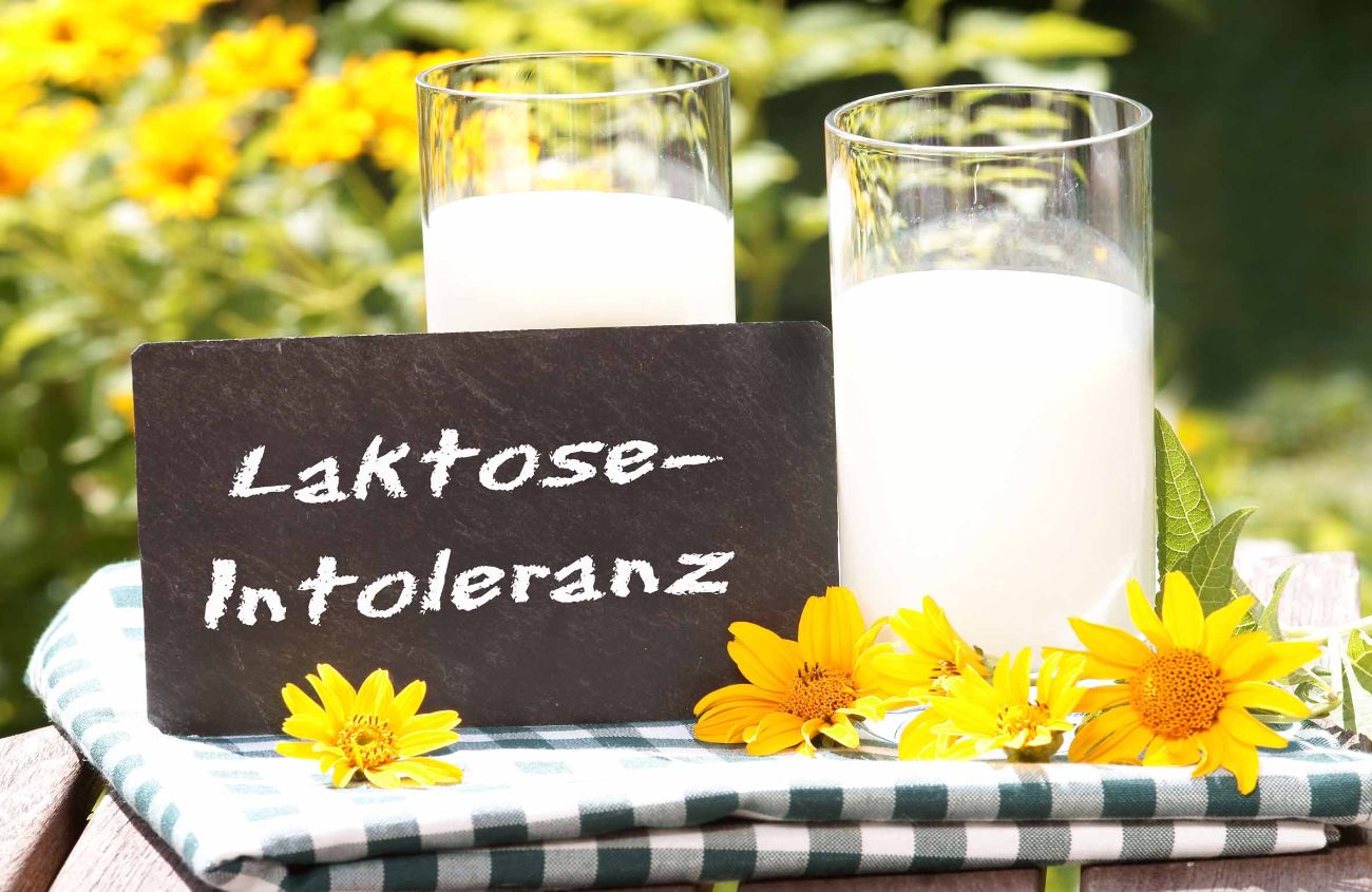 Mögliche Ursache von Sodbrennen, Schriftzug Laktose-Intoleranz neben zwei Gläsern Milch