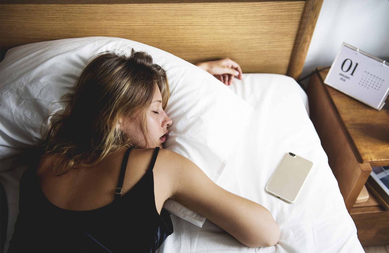 Tipps für gesunden Schlaf, Smartphone liegt neben schlafender Frau im Bett