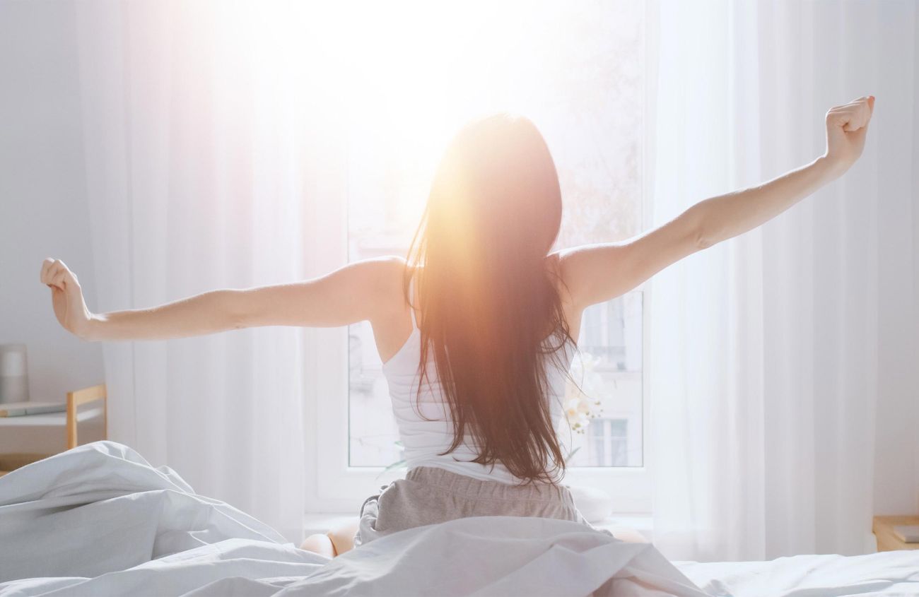 Tipps für gesunden Schlaf, Frau streckt sich im Sonnenaufgang