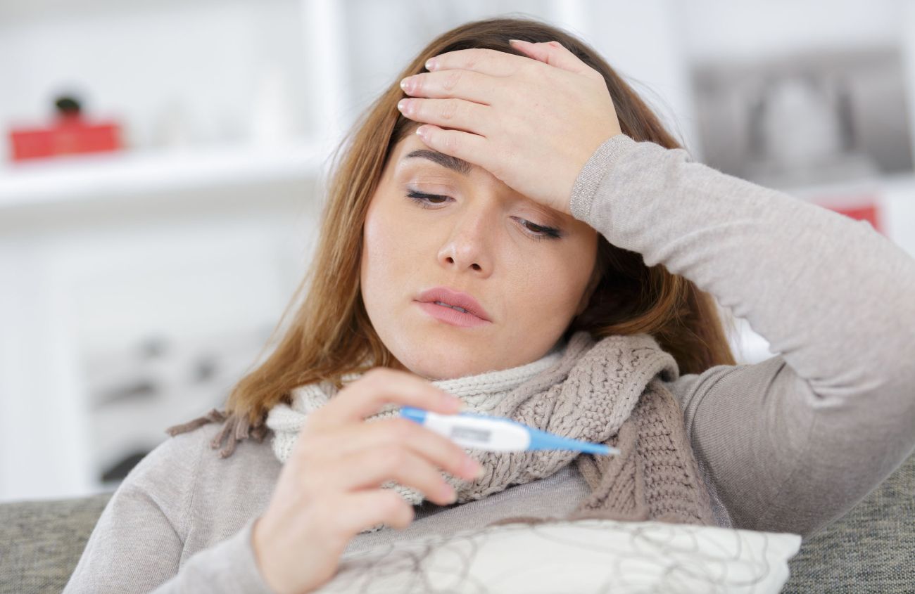 Frau schaut auf ihr Fieberthermometer und hält sich die Stirn.
