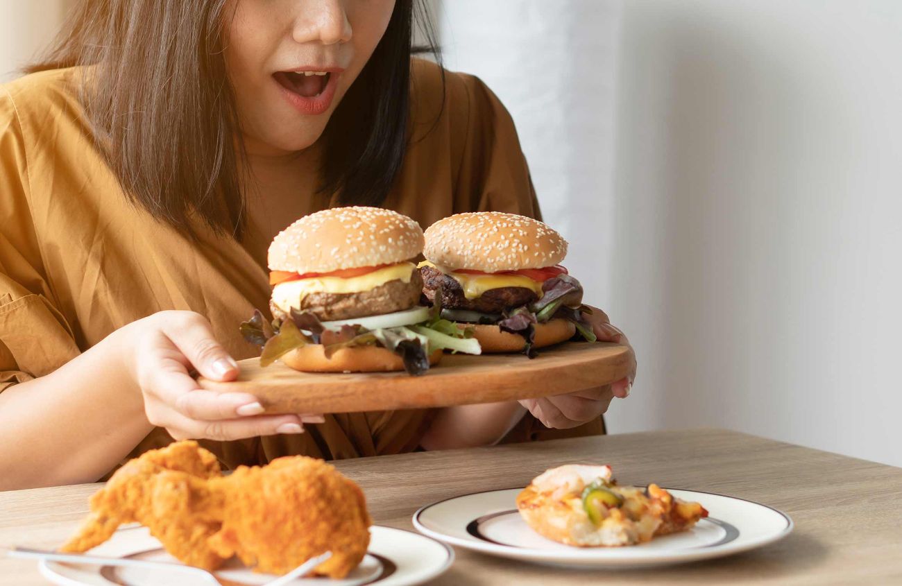 Übergewicht durch Stoffwechselstörung, Frau freut sich auf zwei große Burger