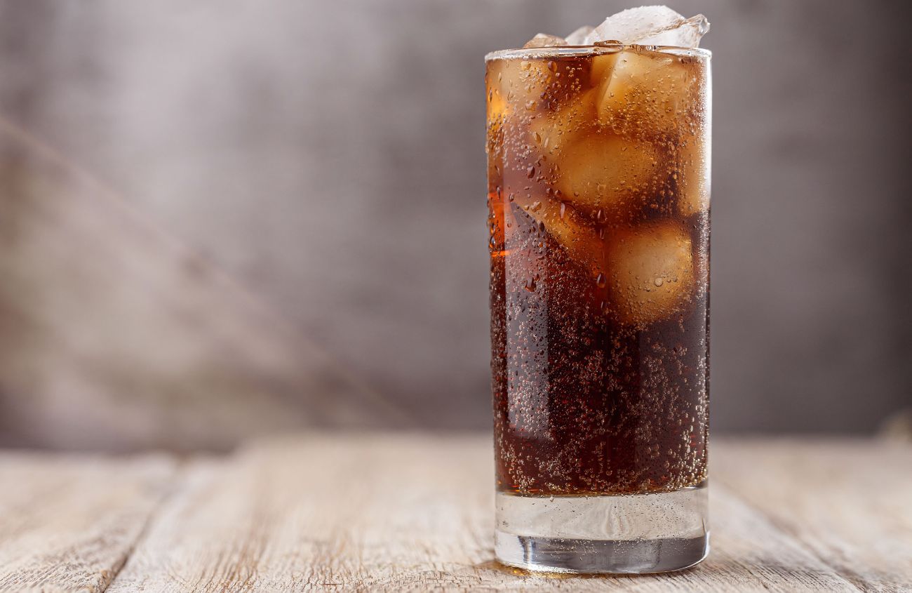 Ein Glas Cola mit Eis auf einem Holztisch.
