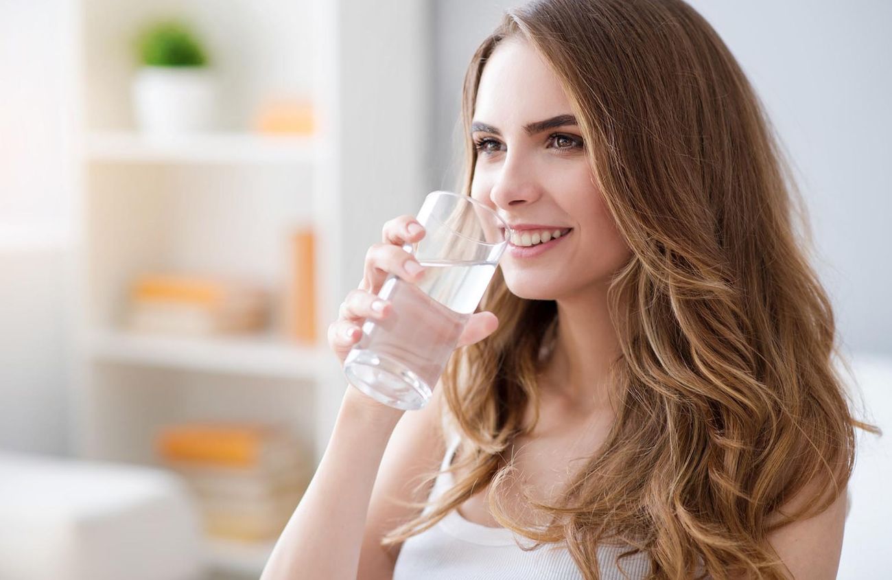 Hausmittel gegen Verdauungsprobleme, Frau trinkt Wasser aus einem Glas