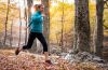 Frau mit blauem Shirt joggt durch den Wald.