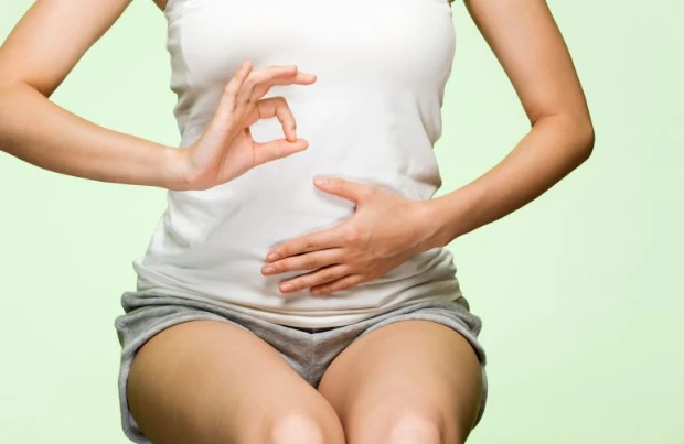 Frau hält sich mit einer Hand den Bauch und formt mit der anderen Hand ein "OK"-Symbol