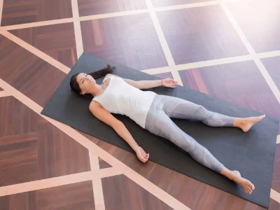 Junge Frau, die auf einem Bretterboden meditiert und in Shavasana-Haltung liegt.