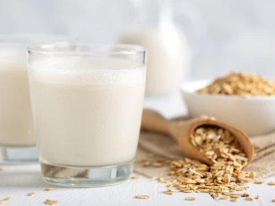 Hafermilch-Unverträglichkeit: Zwei Gläser Milch, daneben Weizenkörner.