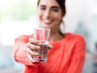 Gewichtszunahme durch zu wenig trinken, Frau hält ein Glas Wasser nach vorne