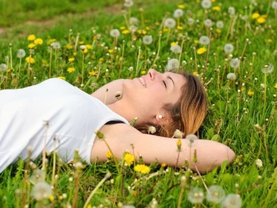 Frau liegt entspannt und lächelnd in einer Blumenwiese