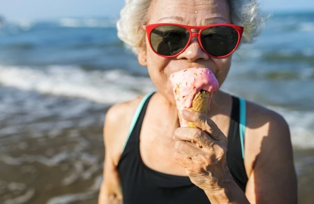 Eine alte Dame isst ein Eis am Strand.