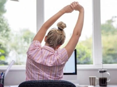 Folgen von Bewegungsmangel, Frau dehnt sich am Schreibtisch