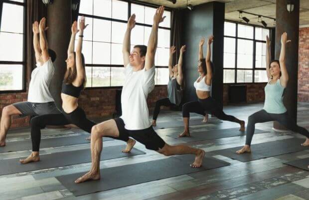 Yoga gegen Verstopfung: Gruppe von jungen sportlichen Leuten in Haltung des Kriegers