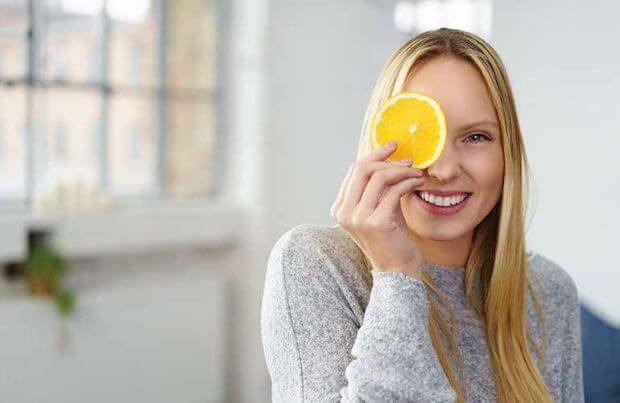 Probiotika für Darmflora und Immunsystem, Frau lacht und hält Orange vor Auge