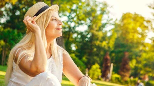 Verdauungsprobleme in den Wechseljahren, Frau mit Hut genießt die Sonne im Freien