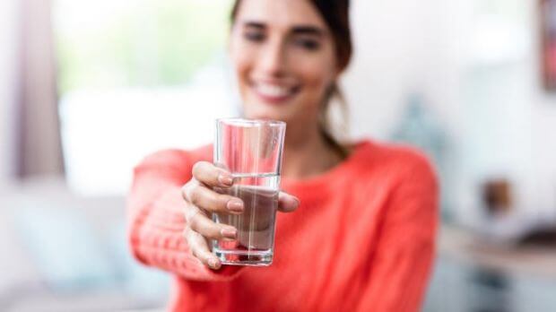 Gewichtszunahme durch zu wenig trinken, Frau hält ein Glas Wasser nach vorne